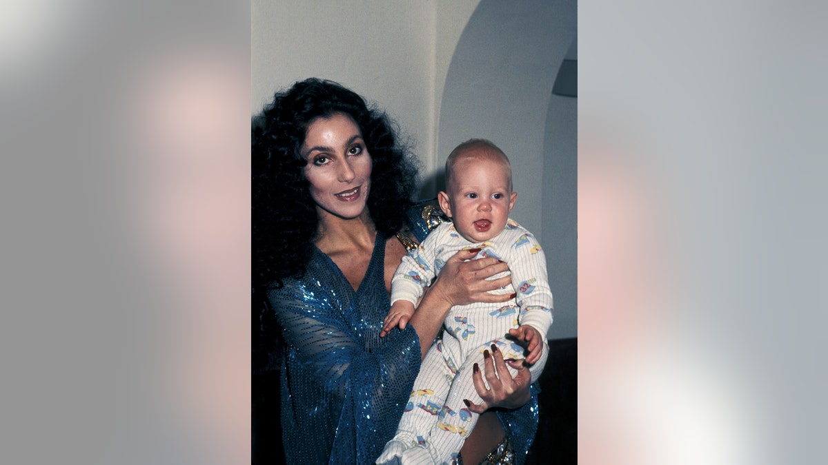 Cher wearing a blue sparkling dress holding her son Elijah Blue