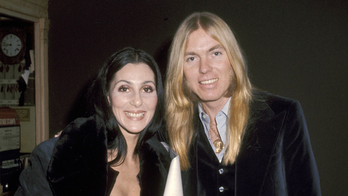 Cher e Gregg Allman sorrindo enquanto olham diretamente para a câmera