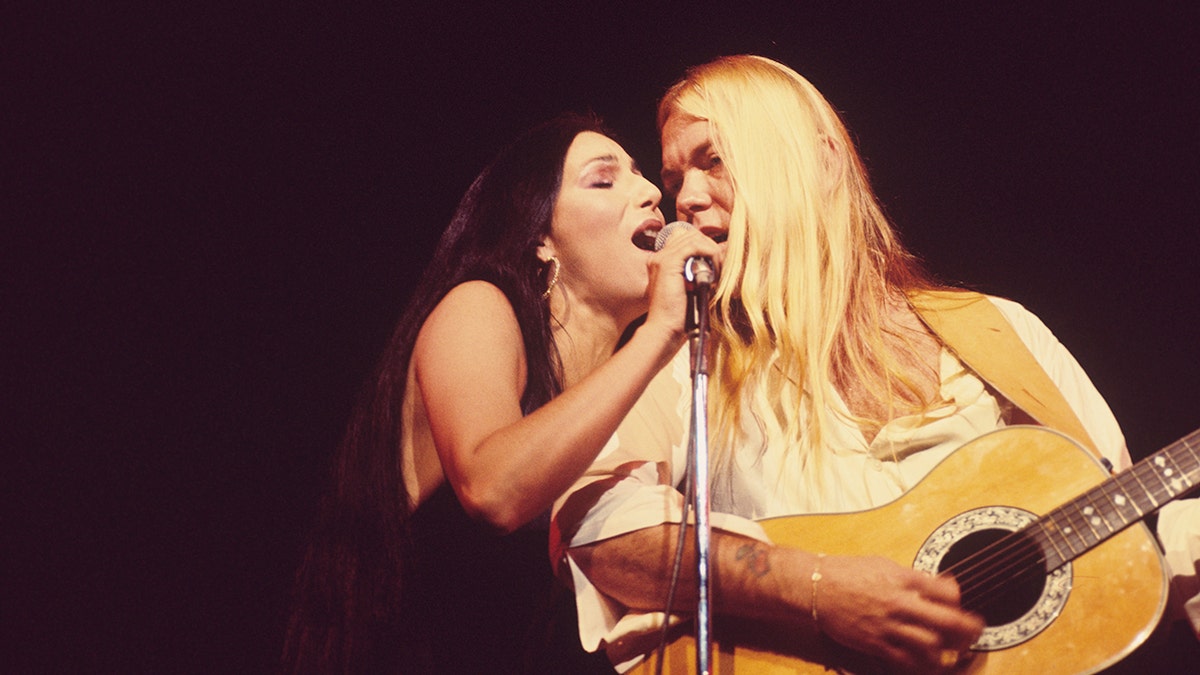 Cher and Gregg Allman performing on stage and sharing a mic