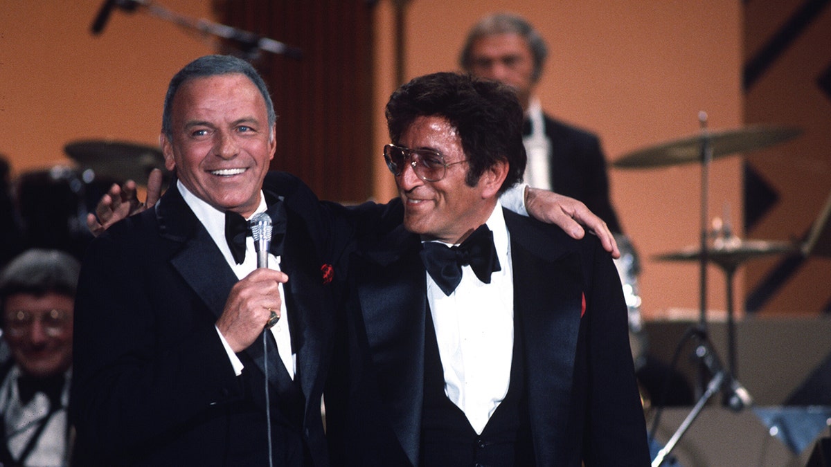 Frank Sinatra embracing Tony Bennett on stage as they both wear suits and bow ties