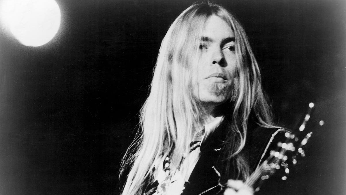A black and white photo of Gregg Allman playing guitar