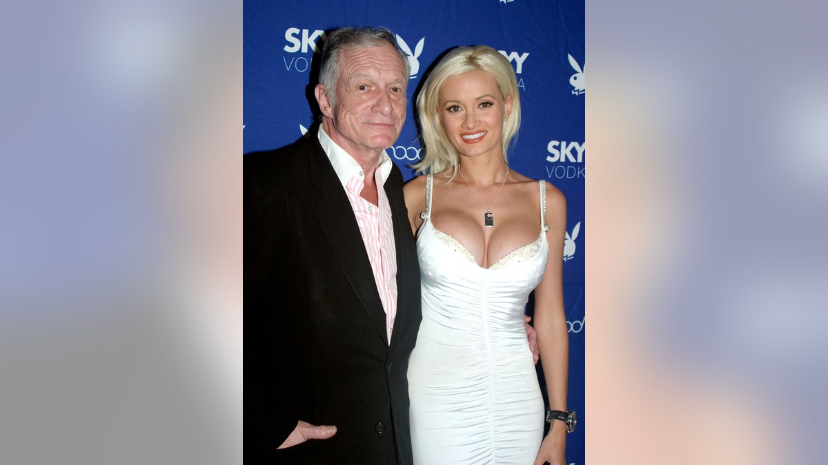 Holly Madison wearing a white dress posing next to Hugh Hefner