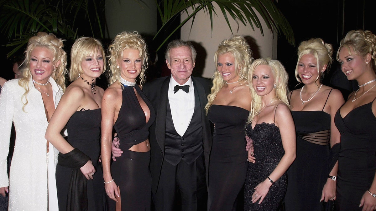 Hugh Hefner in a tux posing with his seven girlfriends wearing black