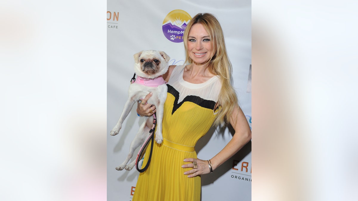 Izabella St. James wearing a yellow and white dress holding a pug