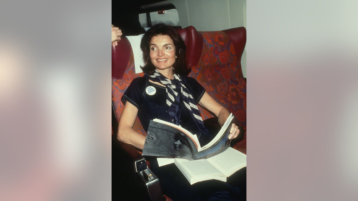 Jackie Kennedy wearing a navy suit holding a book