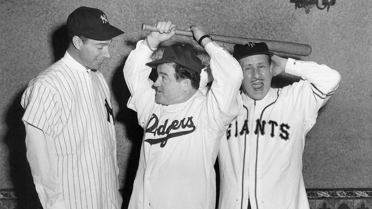 Joe DiMaggio in his baseball uniform looking at Budd Abbott and Lou Costello also in baseball uniforms and holding bats