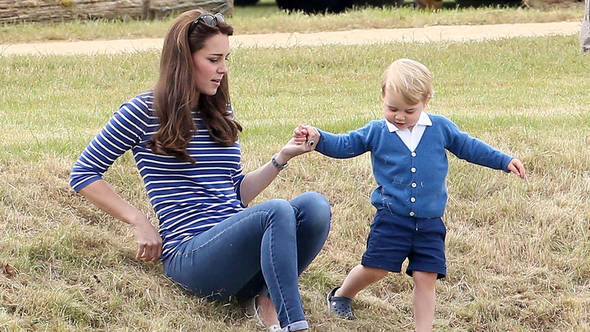 Kate Middleton wearing a striped navy and blue shirt with jeans holding into Prince Georges hand