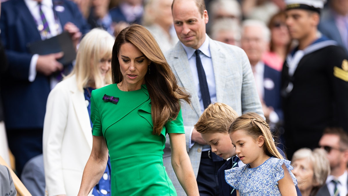Kate Middleton wearing a bright green dress holding onto Prince George and Princess Charlotte