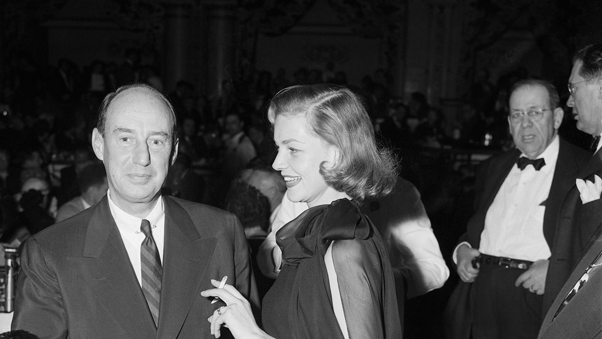 Lauren Bacall wearing a dark dress and smiling next to Adlai Stevenson