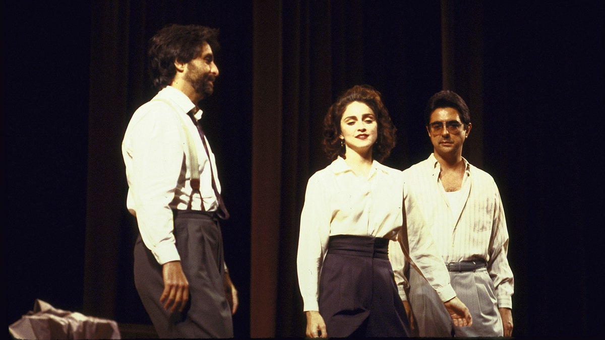 Madonna wearing a white shirt and black slacks in between two actors on stage