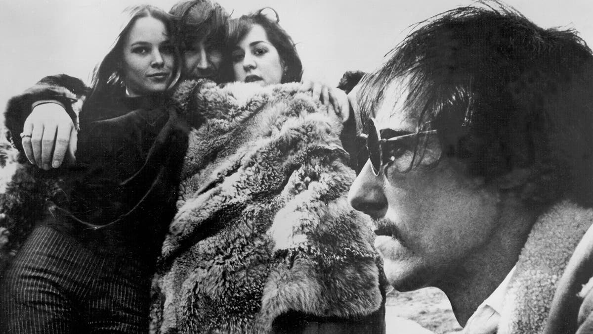 John Phillips looking away as the rest of his band wrap themselves in a fur coat