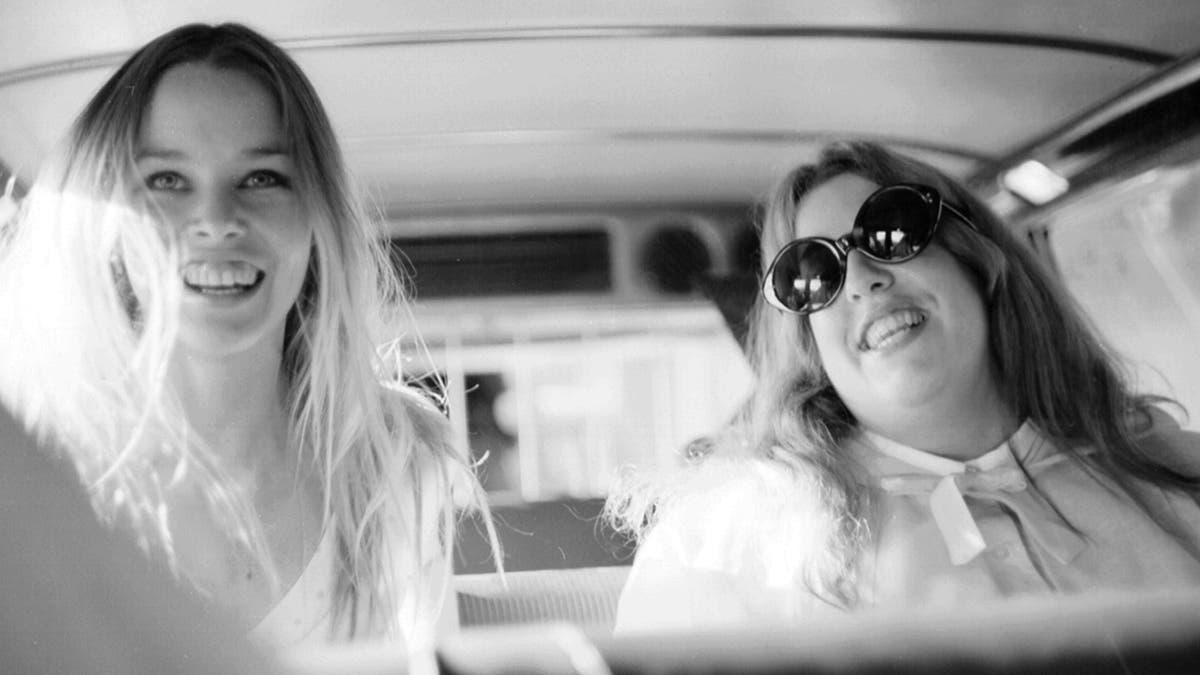Michelle Phillips and Cass Elliot in a car smiling