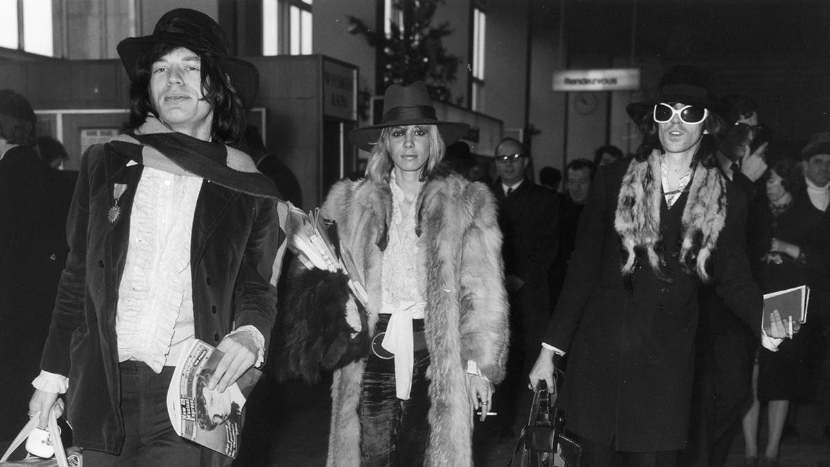 Mick Jagger, Anita Pallenberg and Keith Richards wearing coats and walking together