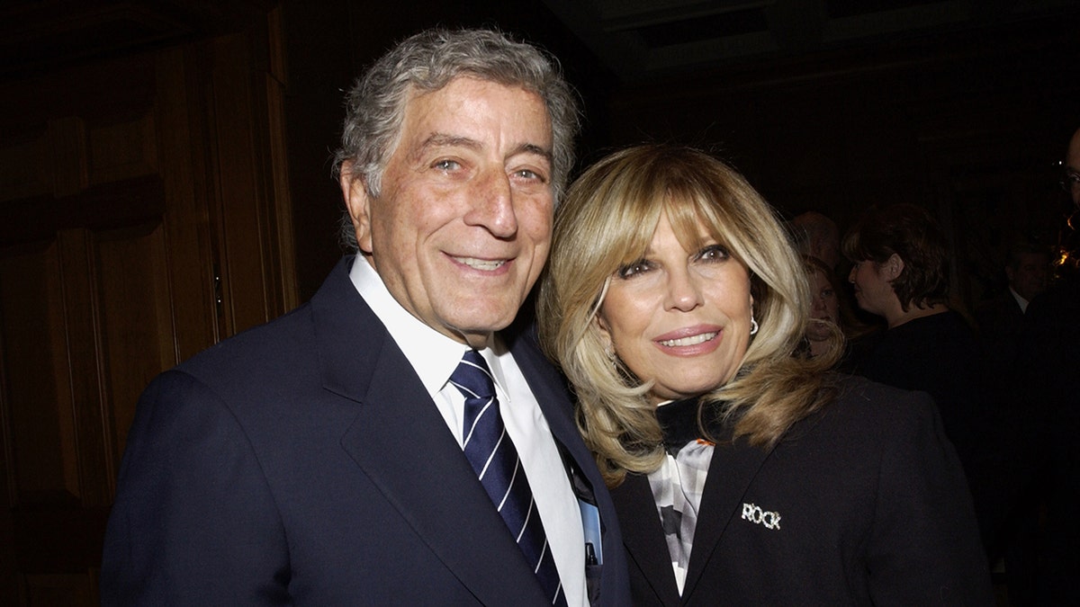 Tony Bennett and Nancy Sinatra leaning onto each other while wearing dark jackets and white shirts
