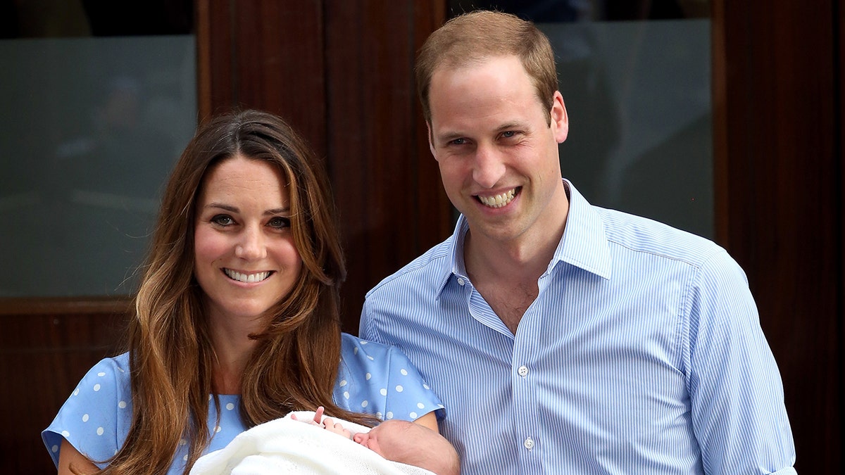Kate Middleton and Prince William wearing light blue outfits holding a newborn Prince George