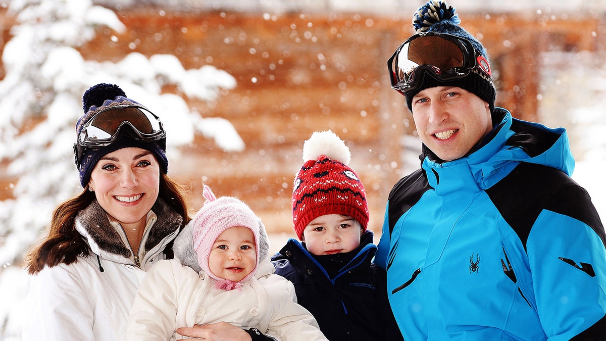 Kate Middleton and Prince William wearing blue and white coats and wool hats while holding their bundled up children