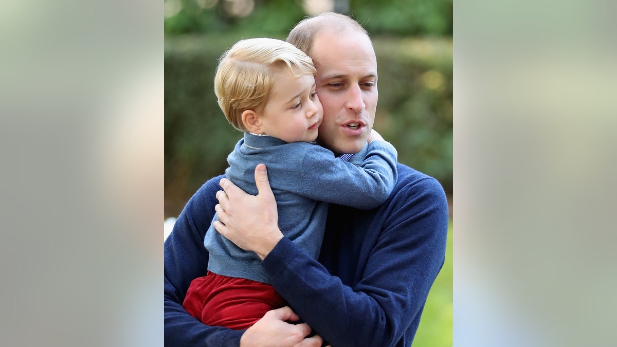 Prince William wearing a blue sweater holding Prince George wearing a matching blue sweater