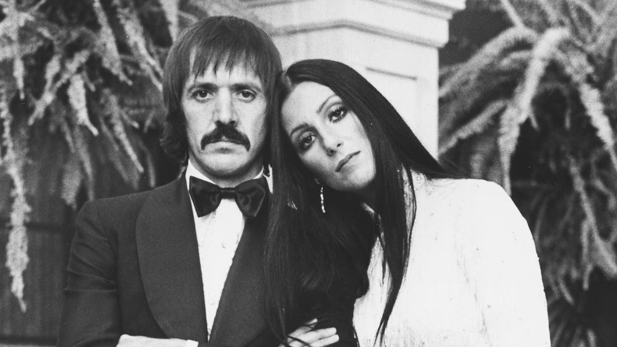 Portrait of singing duo Sonny Bono and Cher, wearing formal dress on an outdoor patio