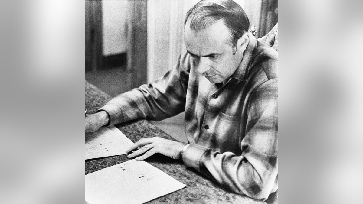 Donald G. Harden wearing a plaid shirt and looking at a stack of papers