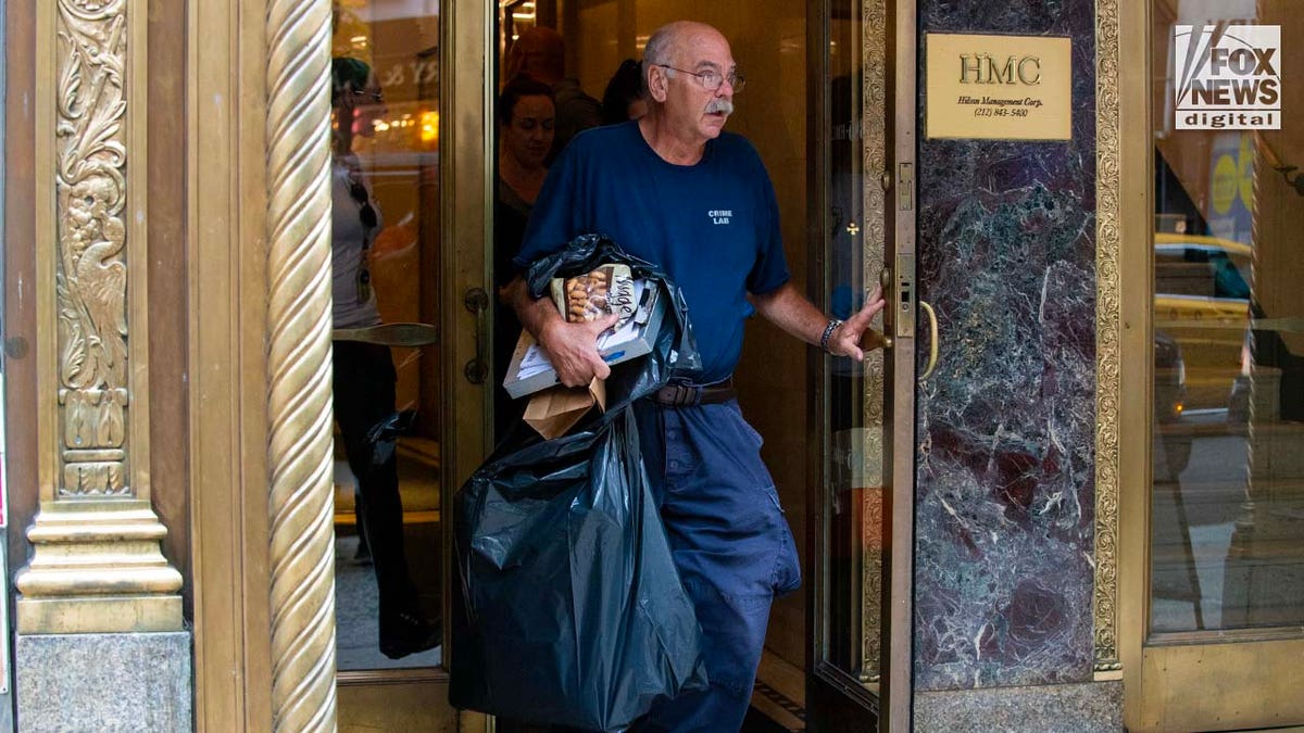 A Suffolk County Crime Lab detective carries items out of 385 Fifth Avenue