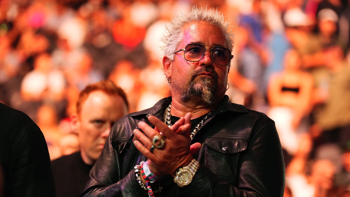 Guy Fieri wearing sunglasses lookin serious while midway through clapping