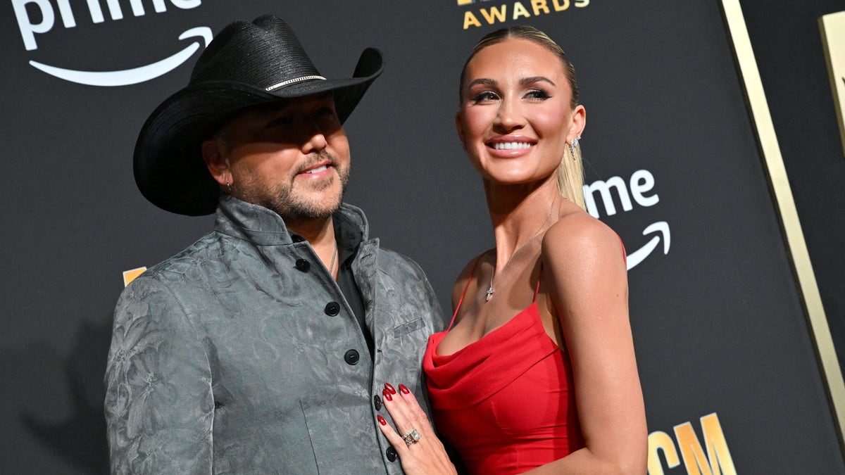 Jason Aldean in a suit and cowboy hat with Brittany Aldean in a red dress