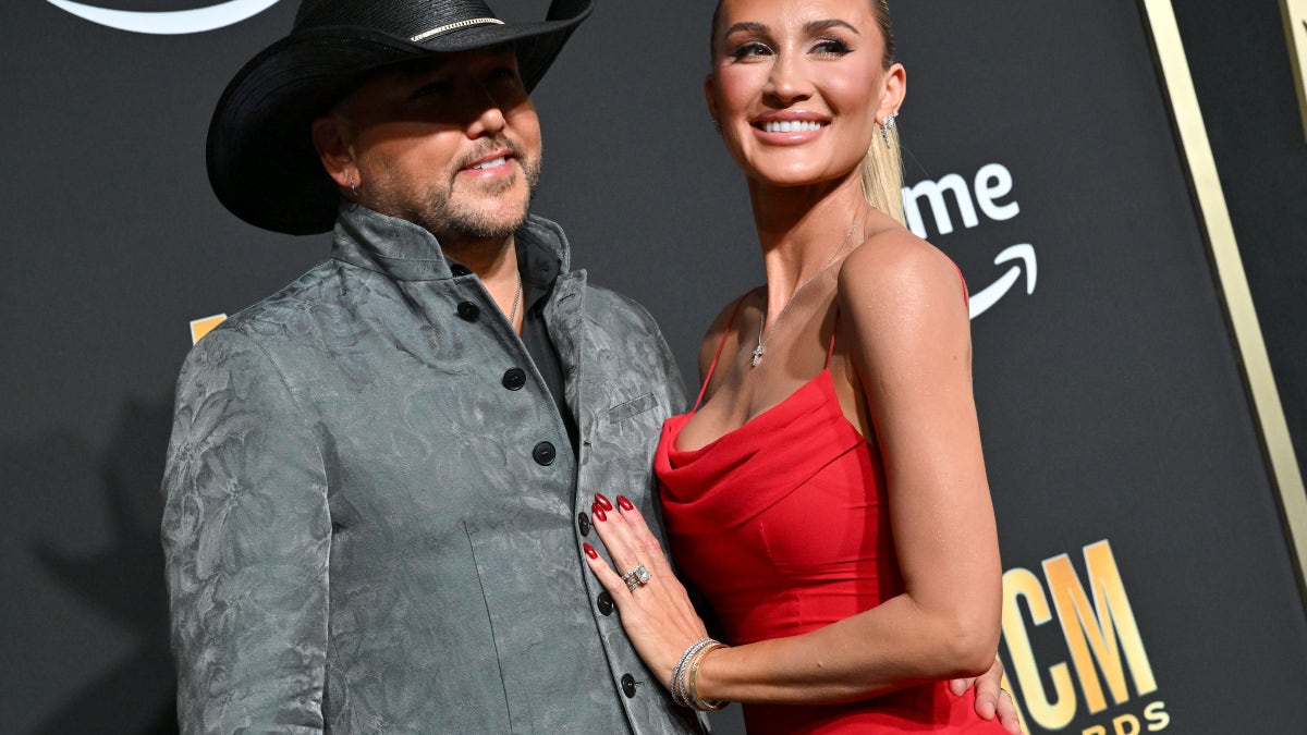 Jason Aldean in a suit and cowboy hat with Brittany Aldean in a red dress