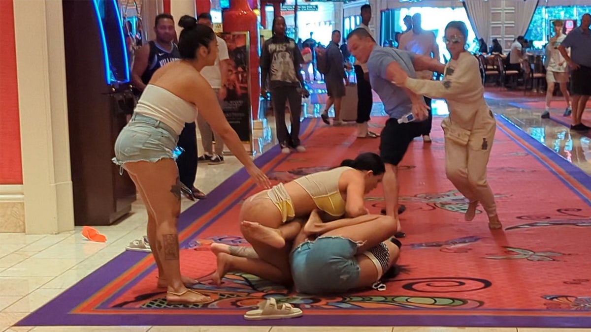 A woman in a thong is shown tussling with a woman in cut off shorts on the floor of a casino.