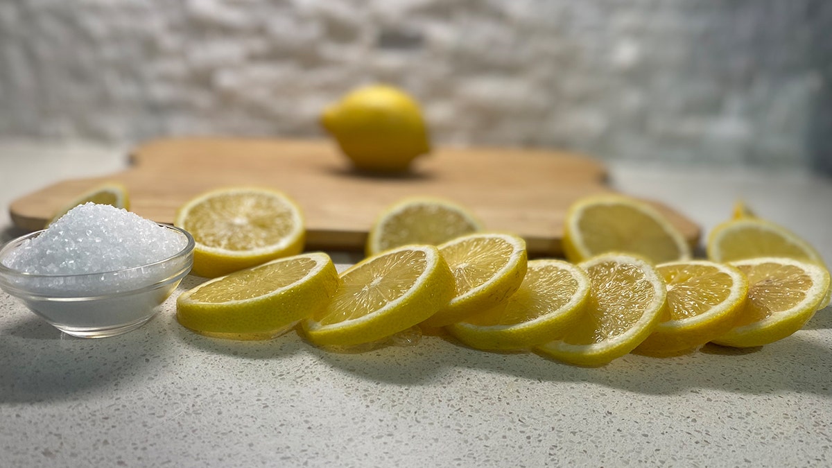 Sliced lemons and sea salt arranged in front of a wood cutting board.