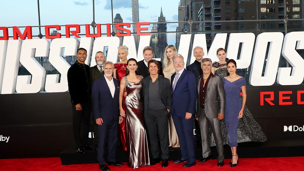 The cast of Mission: Impossible Dead Reckoning Part 1 stand together in a group, including Tom Cruise, Hayley Atwell, Simon Pegg, Rebecca Ferguson, Vanessa Kirby, and director Chris McQuarrie