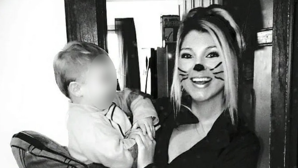 A woman with painted on whiskers holds a baby in a black-and-white photo.
