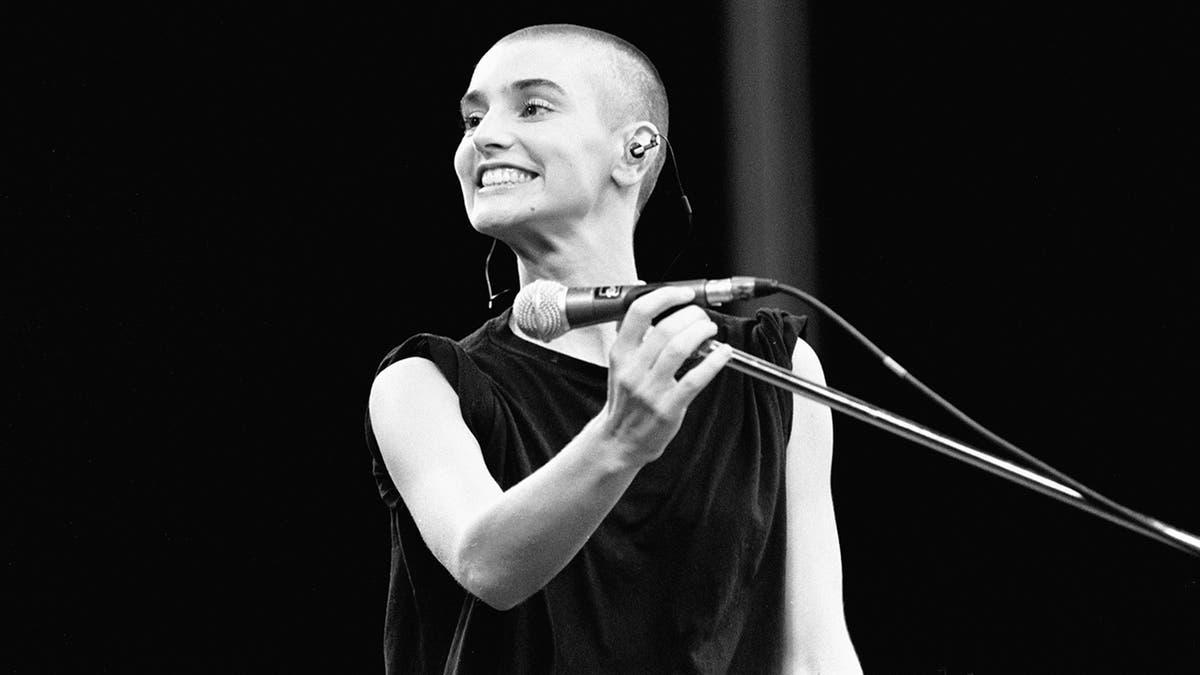 black and white photo of Sinéad O'Connor smiling at the microphone