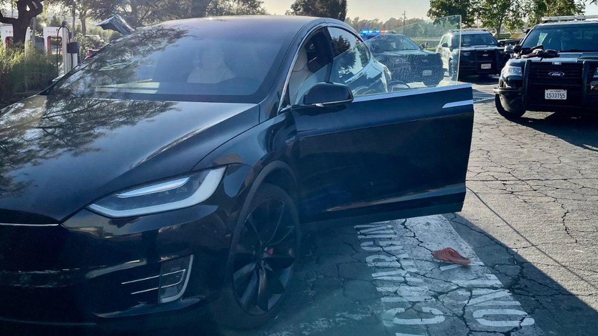 An orange Croc shoe on ground next to stolen black Tesla with door open surrounded by police