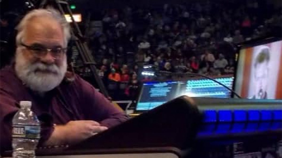 Man at concert sits in front of lighting equipment and two monitors.