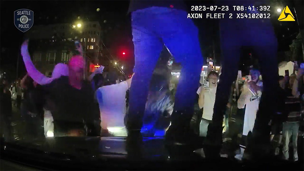 People jumping on the hood of a police unit.
