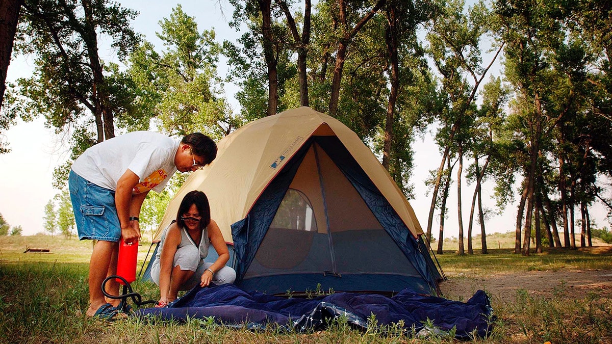 Two people inflating an air mattress outside of a tent 