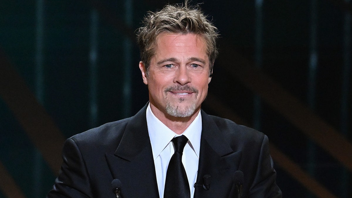 Brad Pitt bites his lower lip and smiles in a black suit