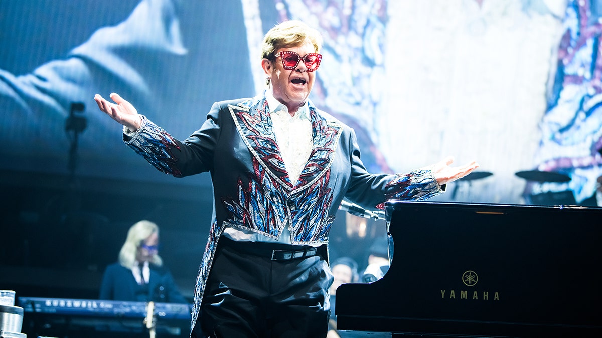 Elton John Stands on stage wearing sunglasses