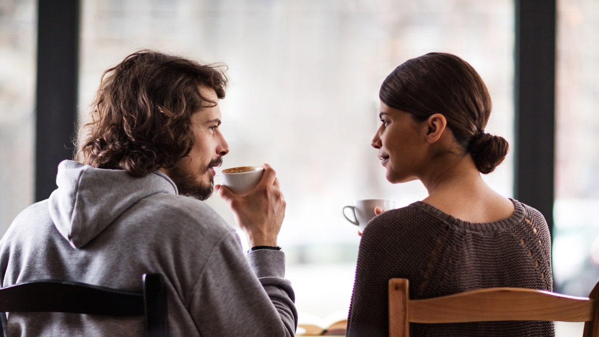 Homem e mulher conversam enquanto tomam café.
