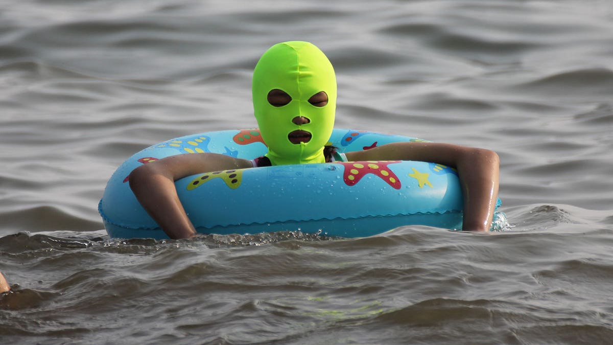 Woman wears green facekini while wading in water