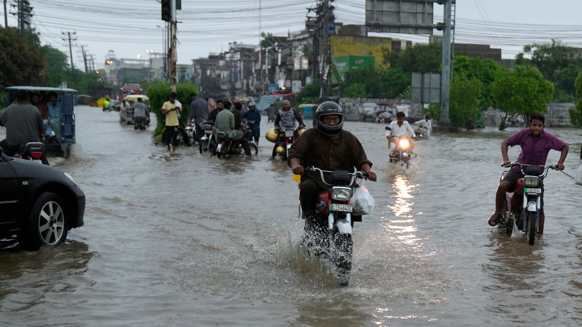 Motorcyclists drive through a flooded roads