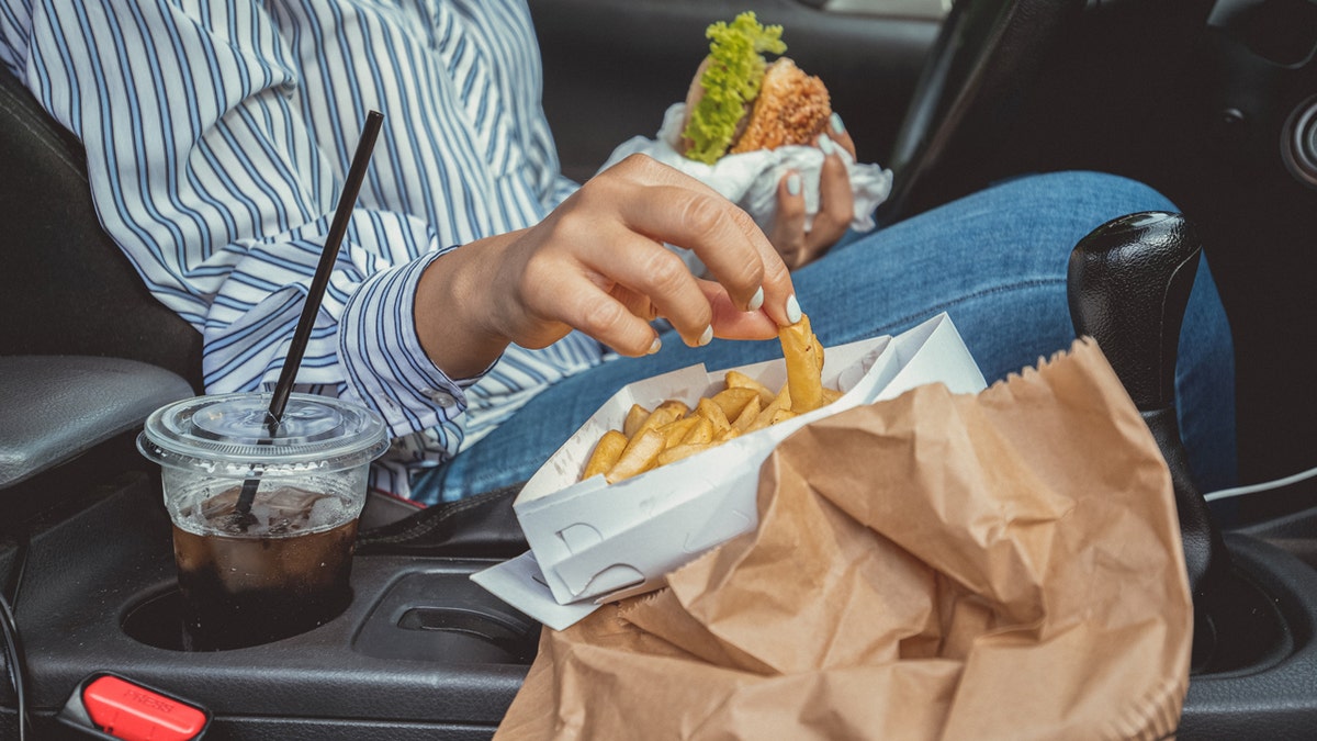 Person eats French fries and burger in car.
