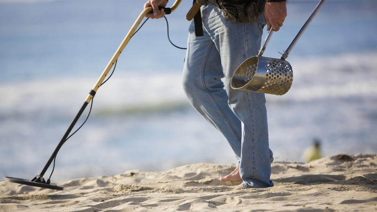 Man searches a beach with a metal detector.