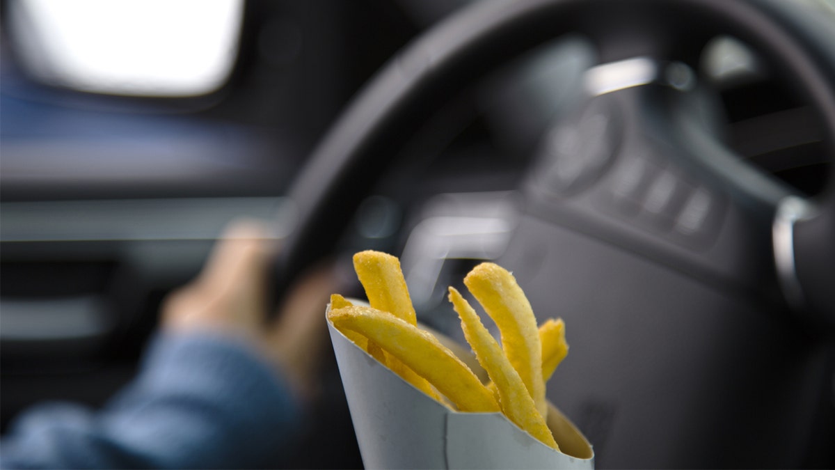 Person holds French fry container while driving.