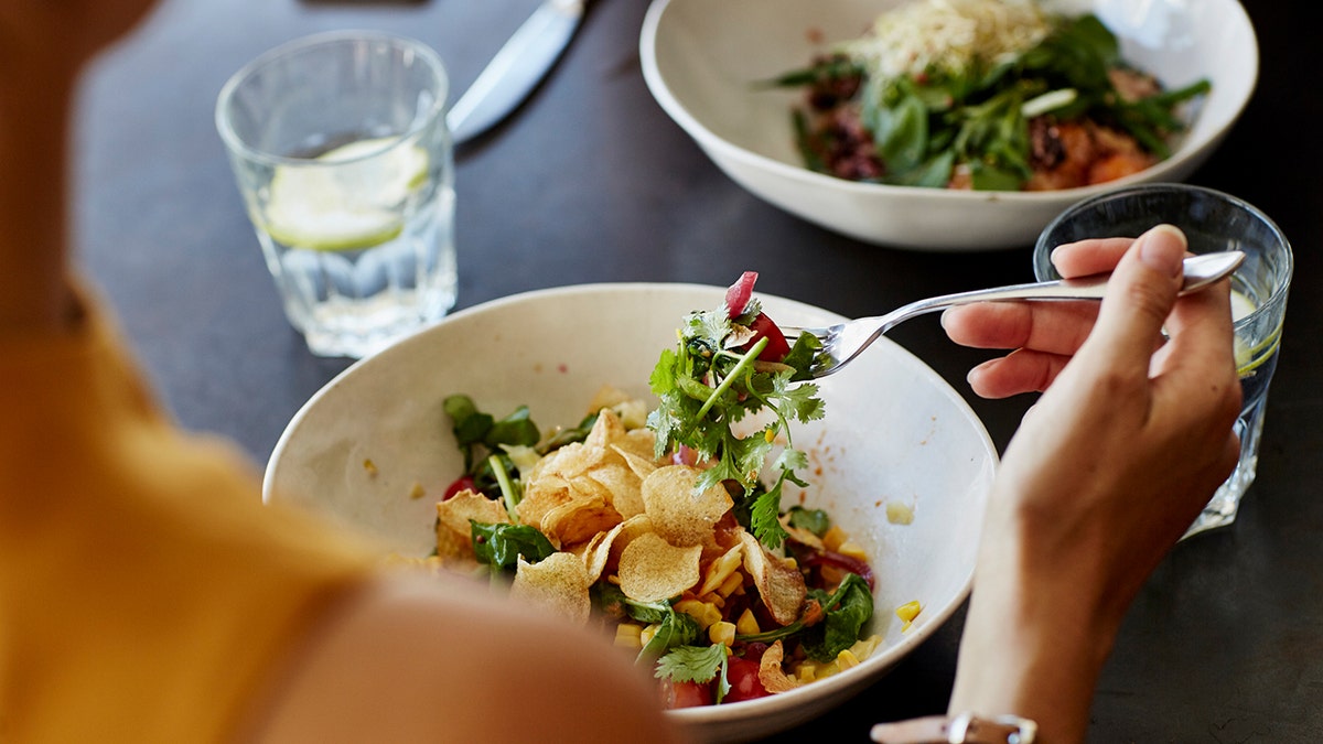 Woman eats healthy meal across from somone.