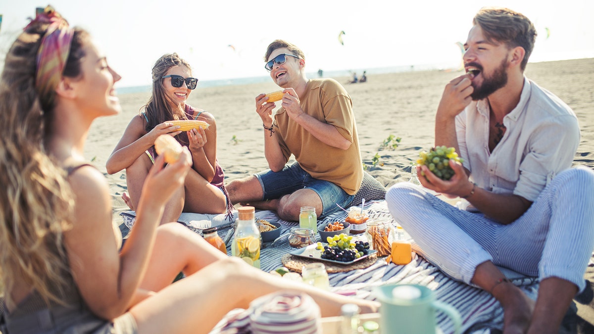People eat while on a beach picnic.
