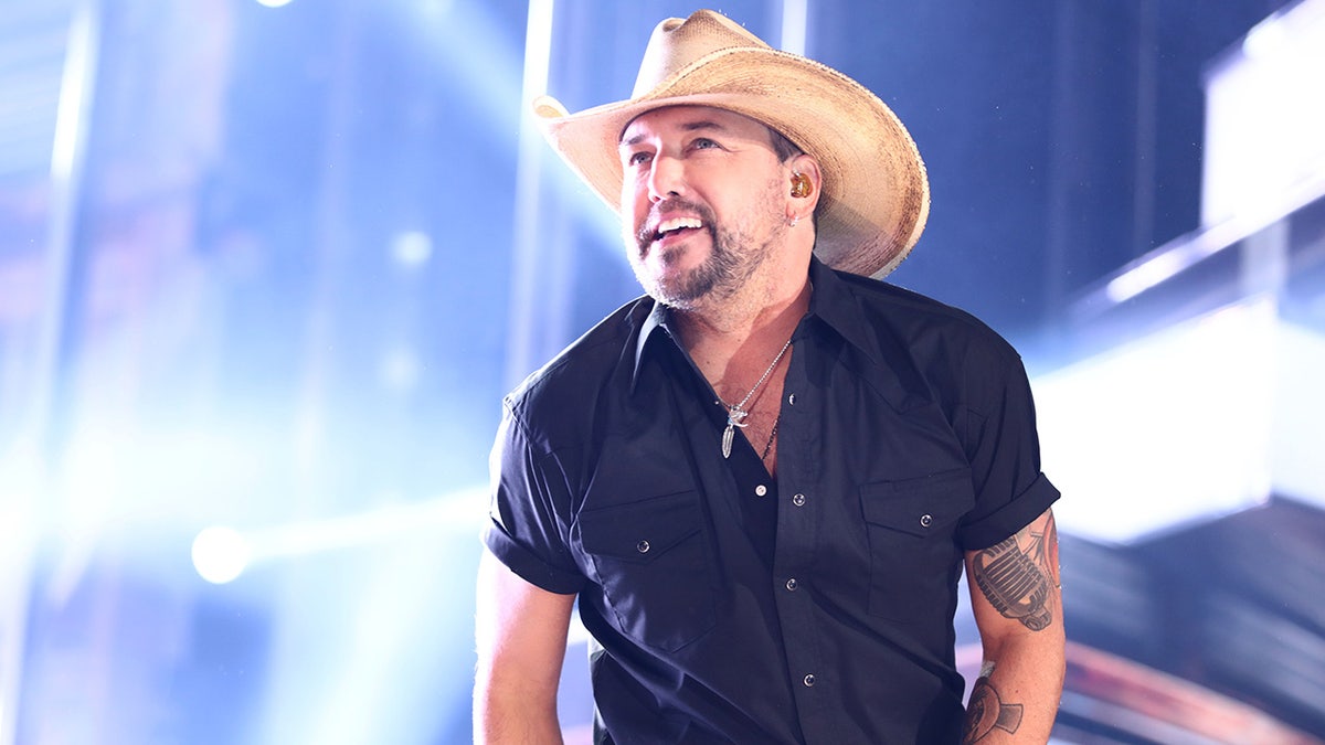 Jason Aldean looks up in a blue shirt and tan cowboy hat while performing