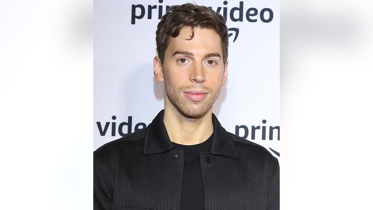 Jordan Gavaris in a black shirt and jacket on the carpet in Canada