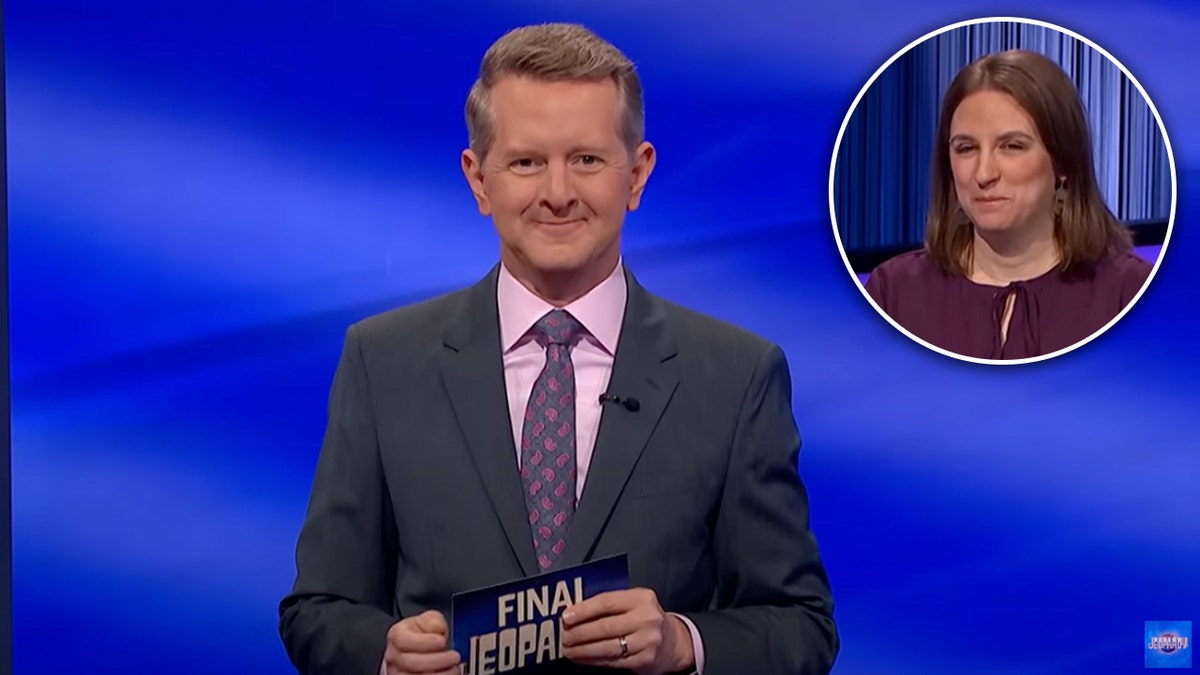 Ken Jennings holds a card on "Jeopardy" wearing a dark suit and a pink shirt with a purple tie