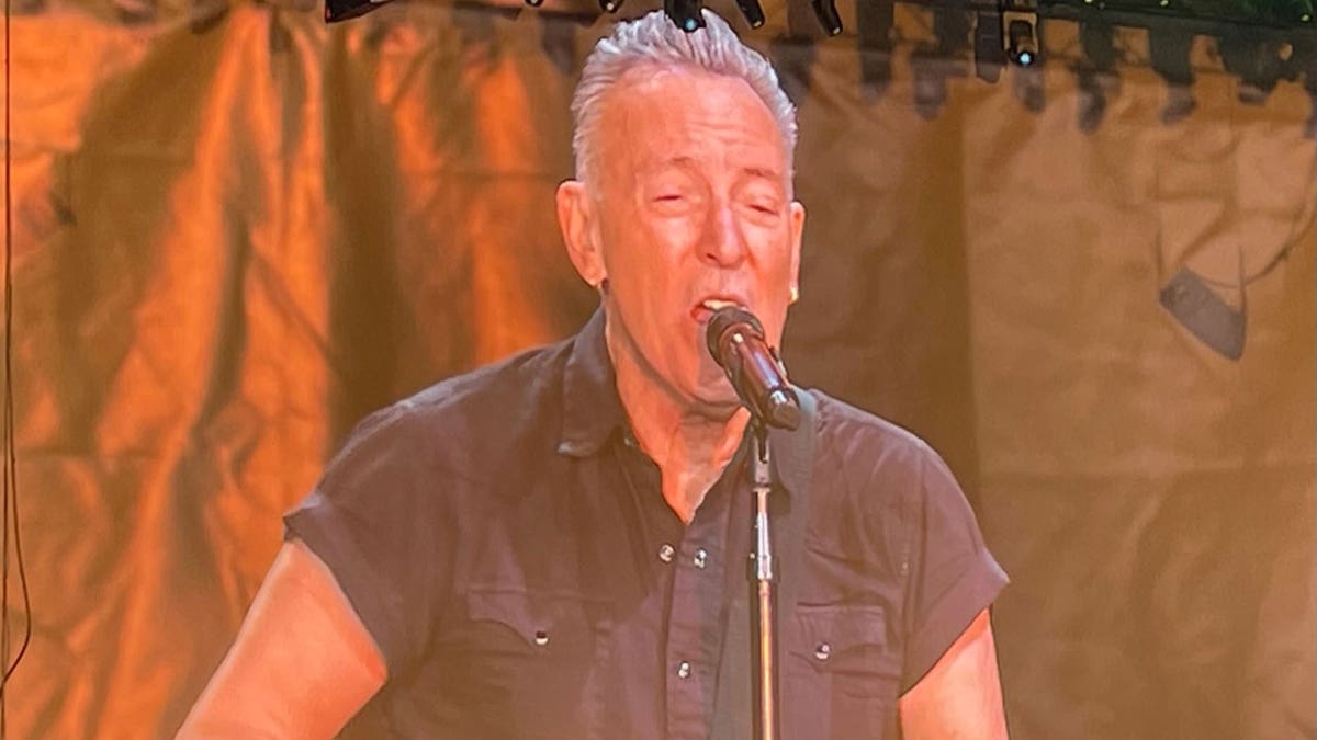 Bruce Springsteen sings into microphone during performance on stage